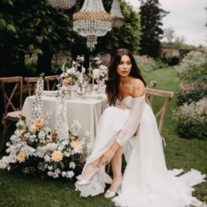 An image of a bride in her wedding gown sitting at a table decorated with flowers