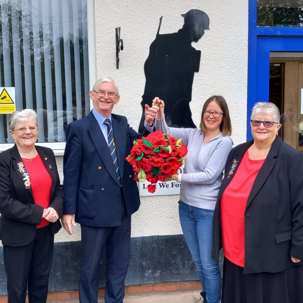 Royal British Legion volunteers standing with representative of Visit Knowle with a knitted basket full of red poppies